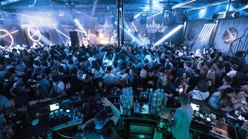 A crowded nightclub with a DJ booth, bar area, and stage lighting.