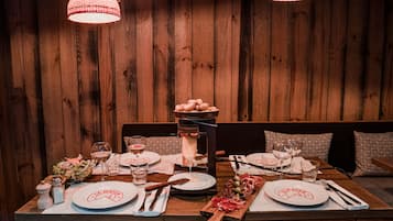 A wooden dining table set with plates, glasses, cutlery, and a wooden board with food.