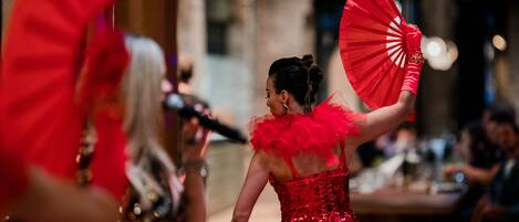A person in a red dress holding a fan, with another person in a sequined dress in the foreground.