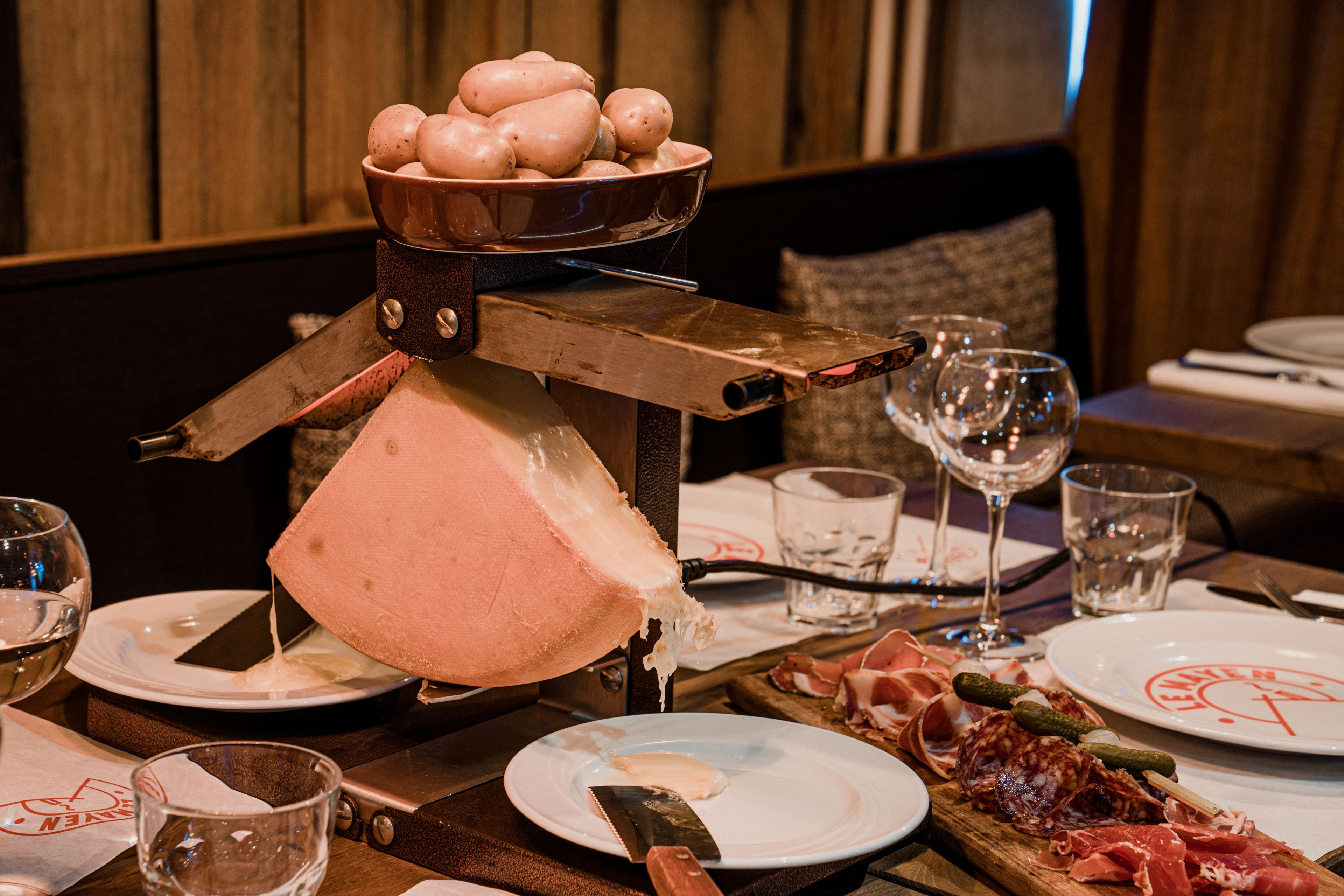 A cheese carving station with a wheel of cheese, a bowl of eggs, and a selection of meats on a wooden board.