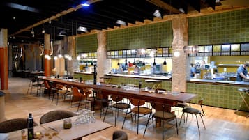 A restaurant with a long wooden table, multiple chairs, and a counter where a chef is preparing food.