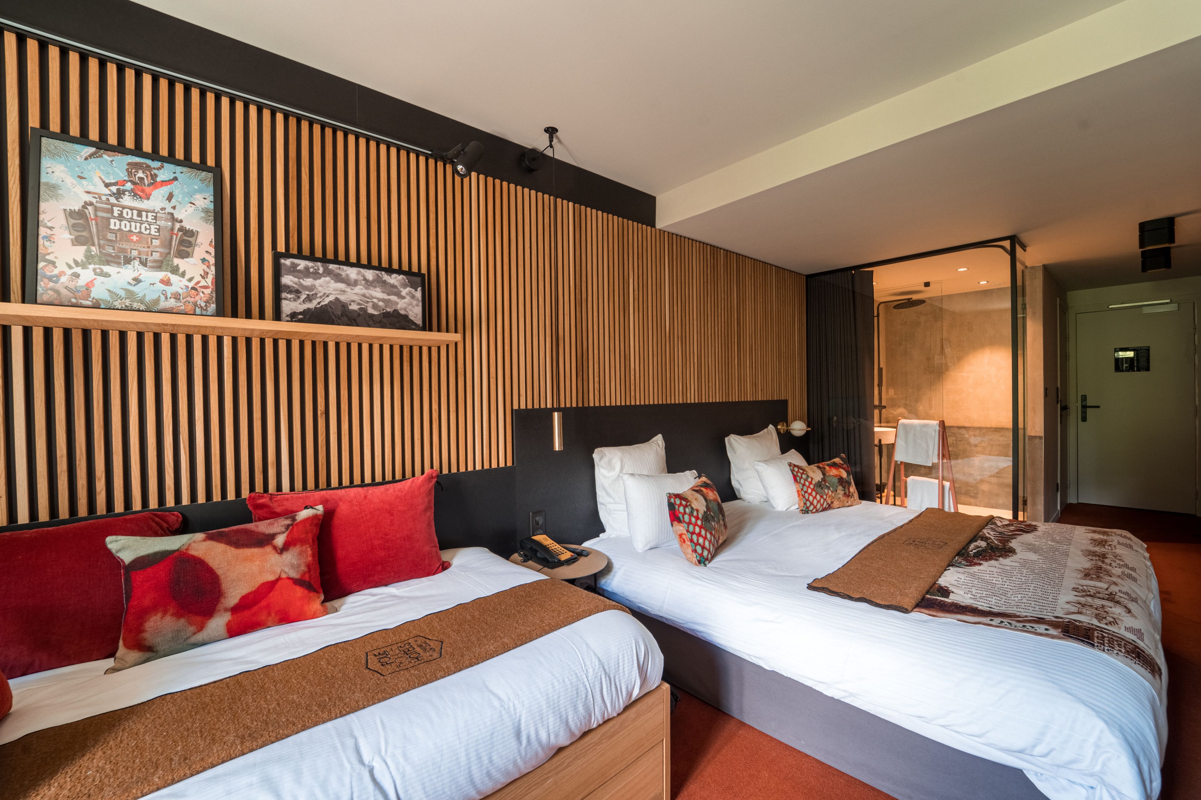 Habitación de hotel con dos camas, paneles de madera en las paredes, un cuadro y un baño visible a través de una puerta abierta.