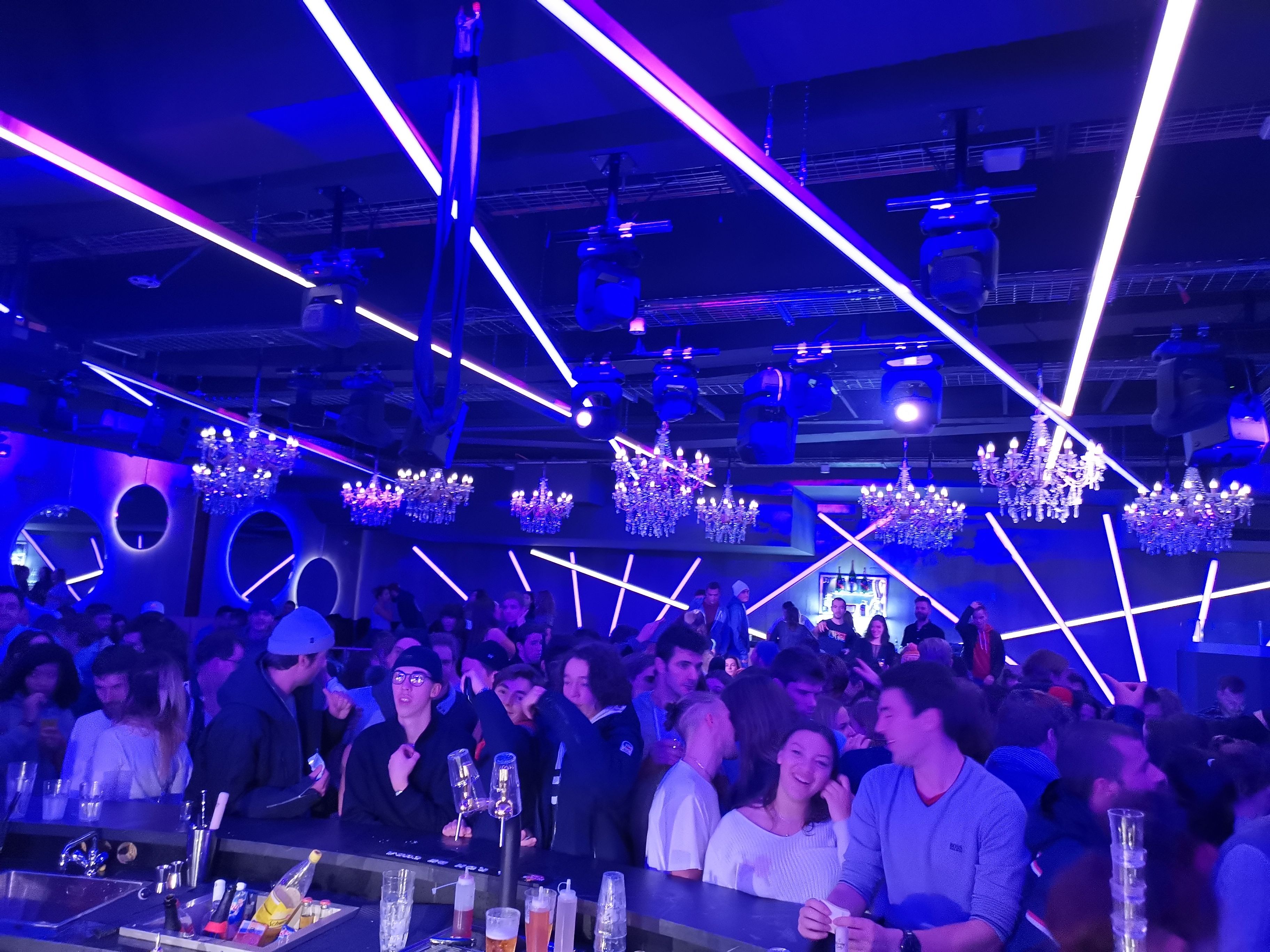 A crowded bar with neon lights and chandeliers.