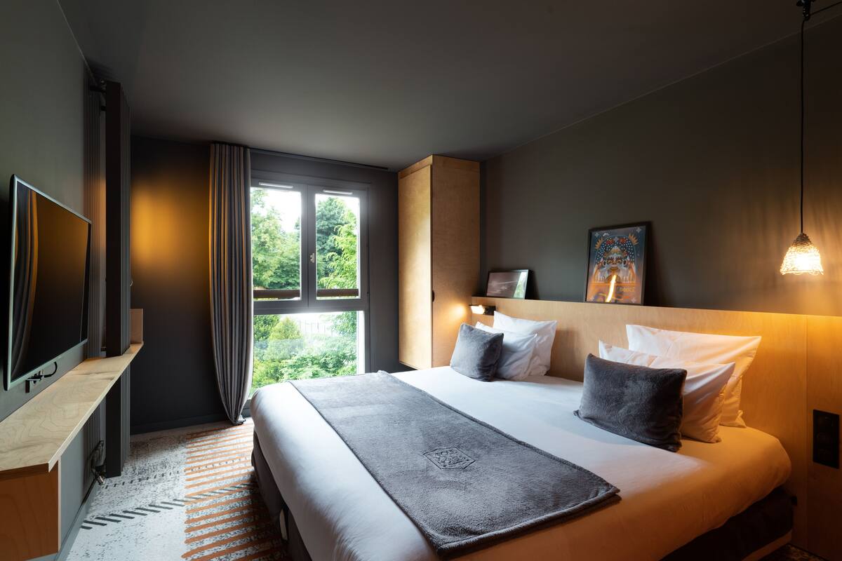 Une chambre d’hôtel moderne dotée d’un grand lit, d’un téléviseur à écran plat et offrant une vue sur la verdure par la fenêtre.
