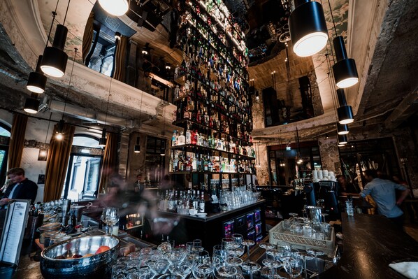 Un bar con techo alto y paredes de ladrillo visto, lleno de botellas y vasos.