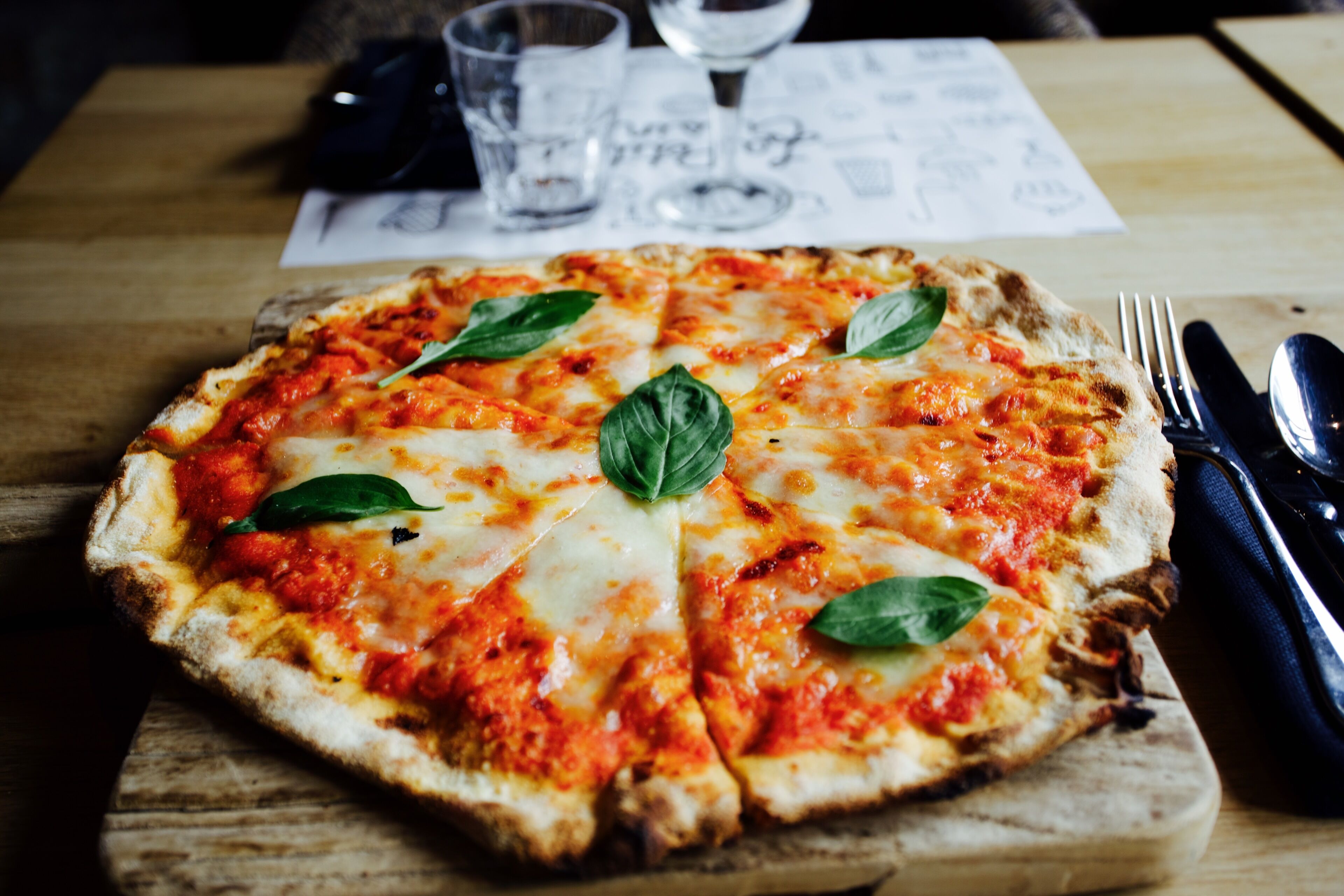 Pizza op een houten plank met vork en mes ernaast.