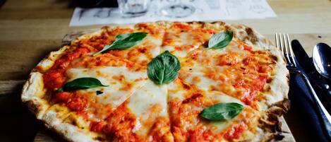 Una pizza sobre una tabla de madera con un tenedor y un cuchillo a un lado.