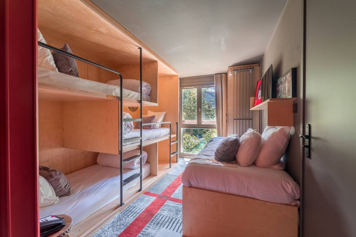 Une pièce compacte avec des lits superposés, un canapé et une fenêtre donnant sur un espace verdoyant.