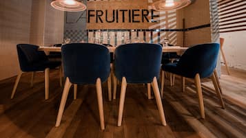 Un coin repas avec une table en bois, des chaises bleues et une enseigne indiquant « FRUITIERE ».