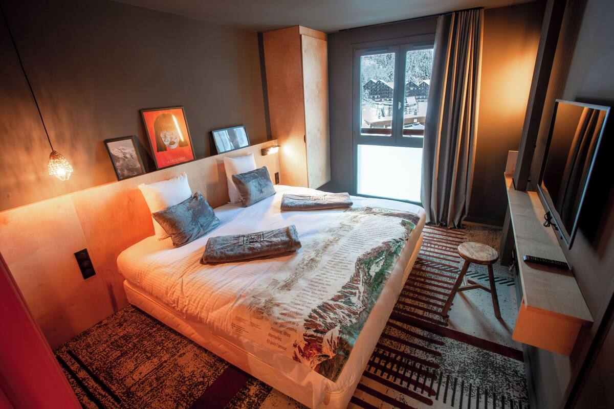 Une chambre à coucher avec un grand lit, un bureau, une chaise, une télévision et une fenêtre avec des rideaux.