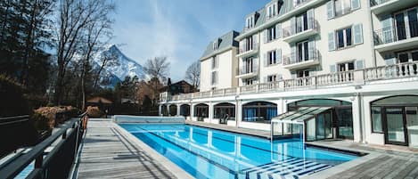Un hotel con piscina, terraza de madera y vistas a la montaña.