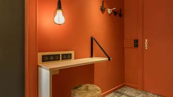 A room with an orange wall, a wooden desk with a light fixture, a stool, and a door with a handle.