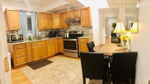 A kitchen with wooden cabinets, a microwave, an oven, and a dining area with a table and chairs. - 4BR 2Baths WOLLASTON BEACH.15min to Boston2 (Quincy)