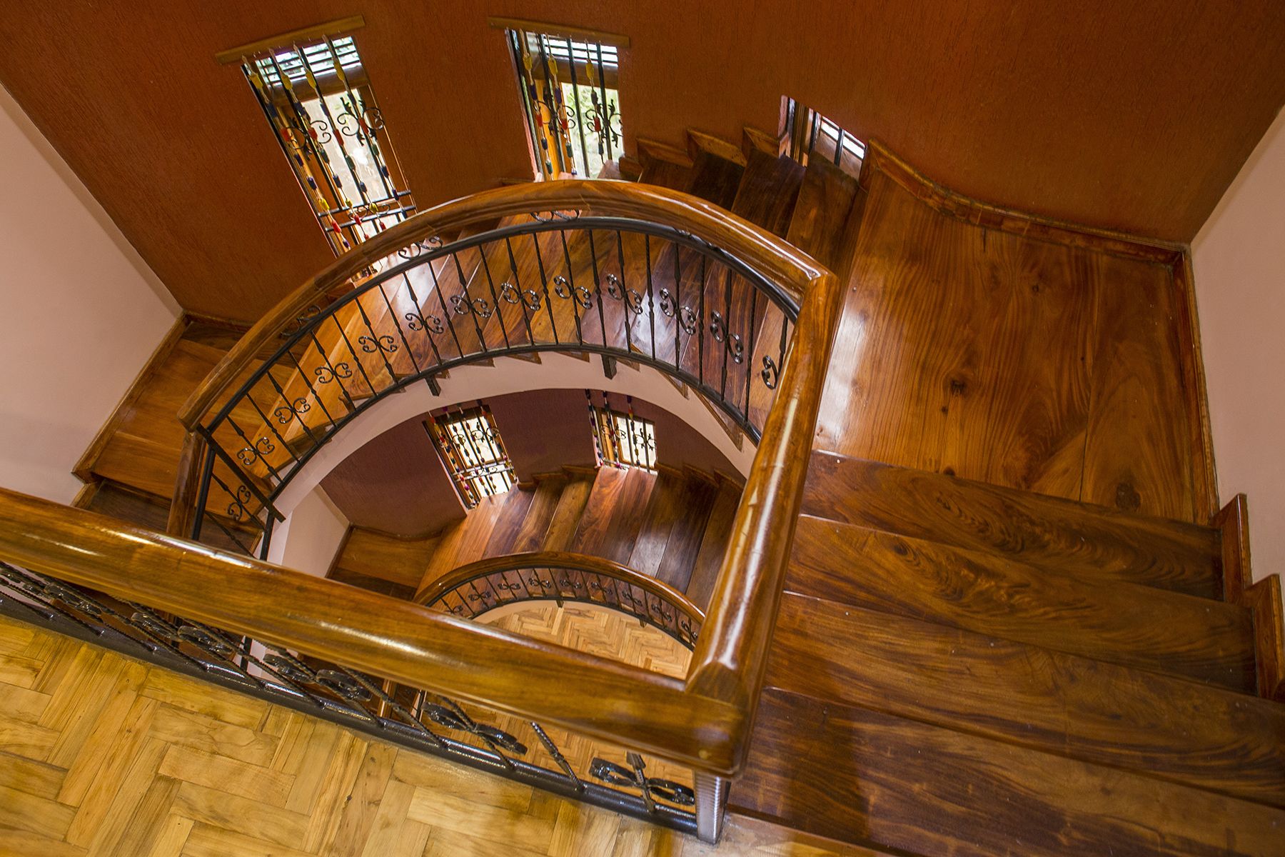 A wooden spiral staircase with ornate metal railings and stained glass windows.