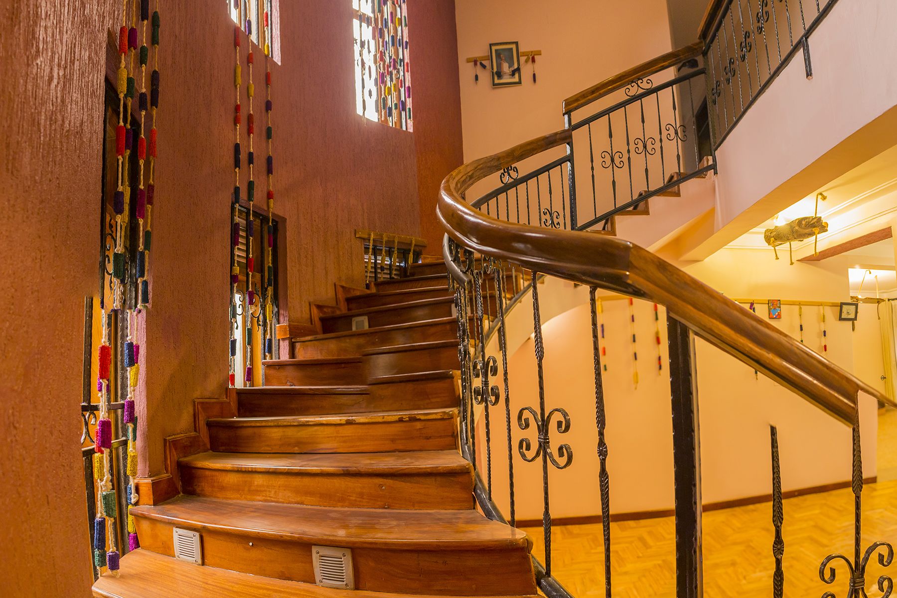 Una escalera de madera con barandales de metal ornamentados y flecos de colores colgando de la pared.