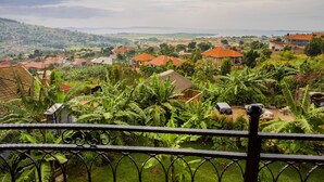 A residential area with houses, a view of a distant landscape, and a metal fence in the foreground. - Dawilderness Holiday Homes (Kampala)