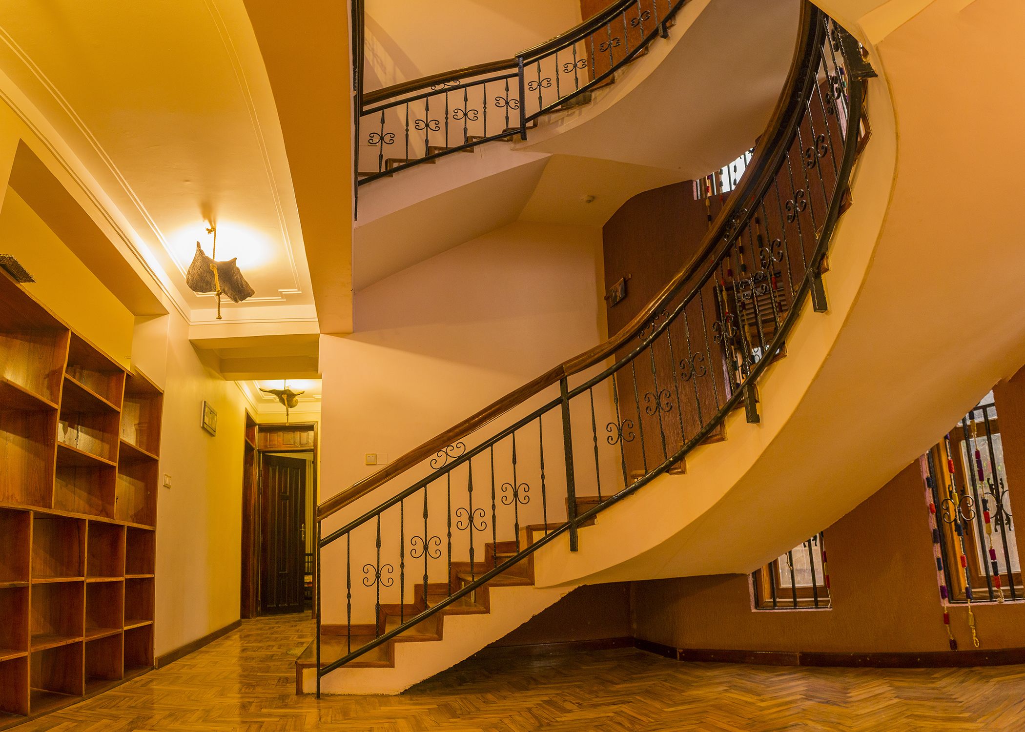 Un magnifique escalier en colimaçon, agrémenté de rampes en métal ouvragé, doté d’un plancher en bois et d’un mur jaune aux tons chaleureux.