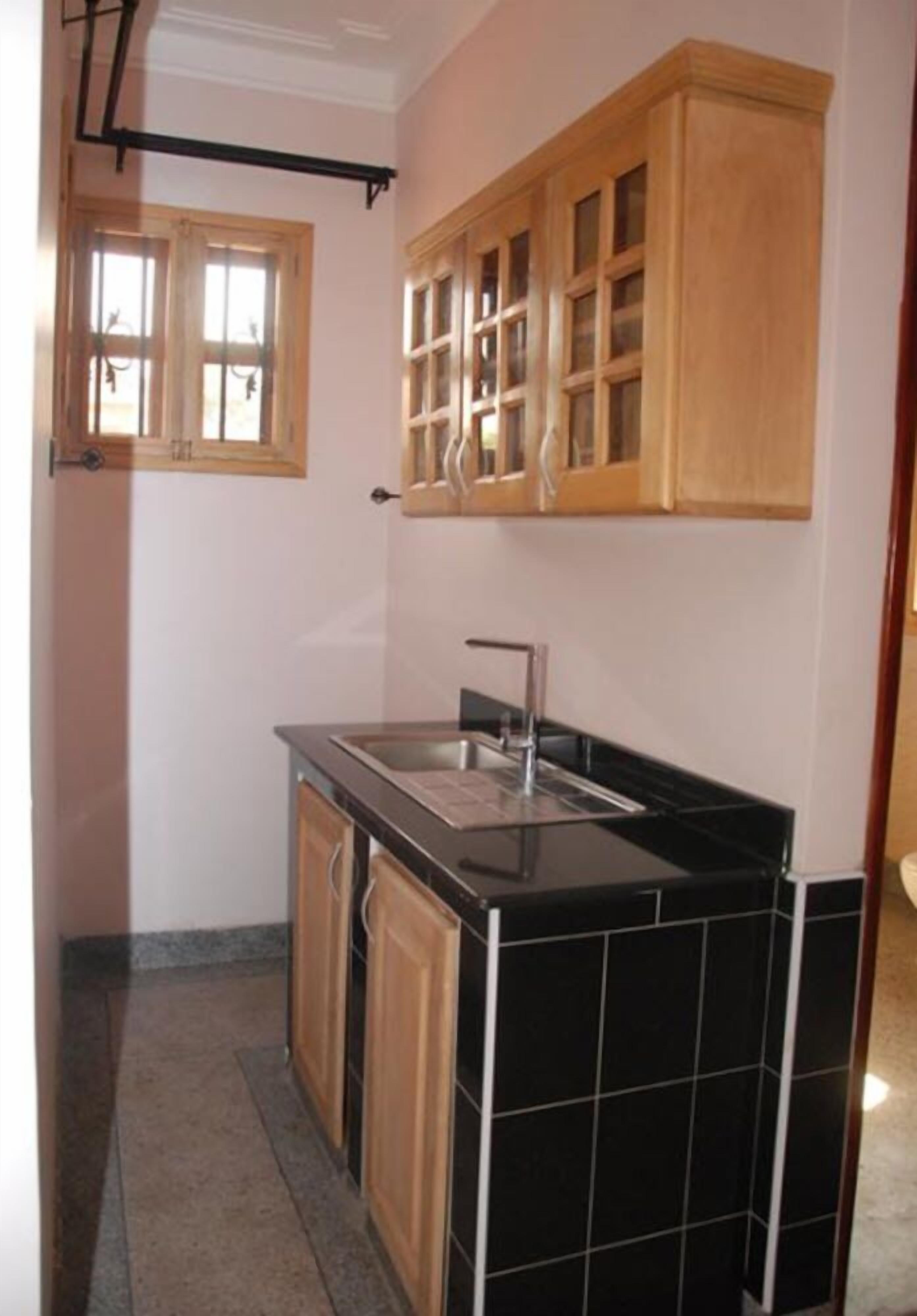 Cocina compacta con encimera negra, armarios de madera y ventana con marcos de madera.