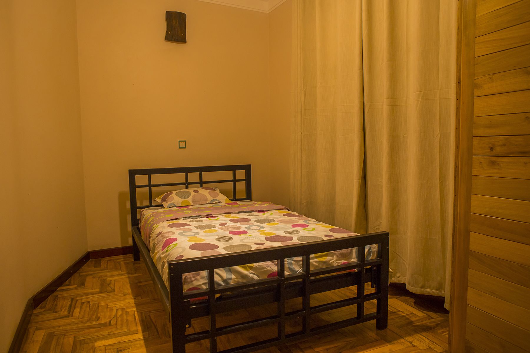 Una habitación pequeña con cama individual, cabecera de madera, colcha estampada y suelo de madera.