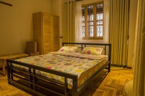 A bedroom with a wooden bed frame, a large window with curtains, and a wardrobe. - Dawilderness Holiday Homes (Kampala)