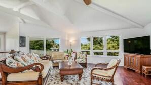 Amplia sala de estar con un televisor grande, muebles de madera y vistas a zonas verdes a través de las ventanas.