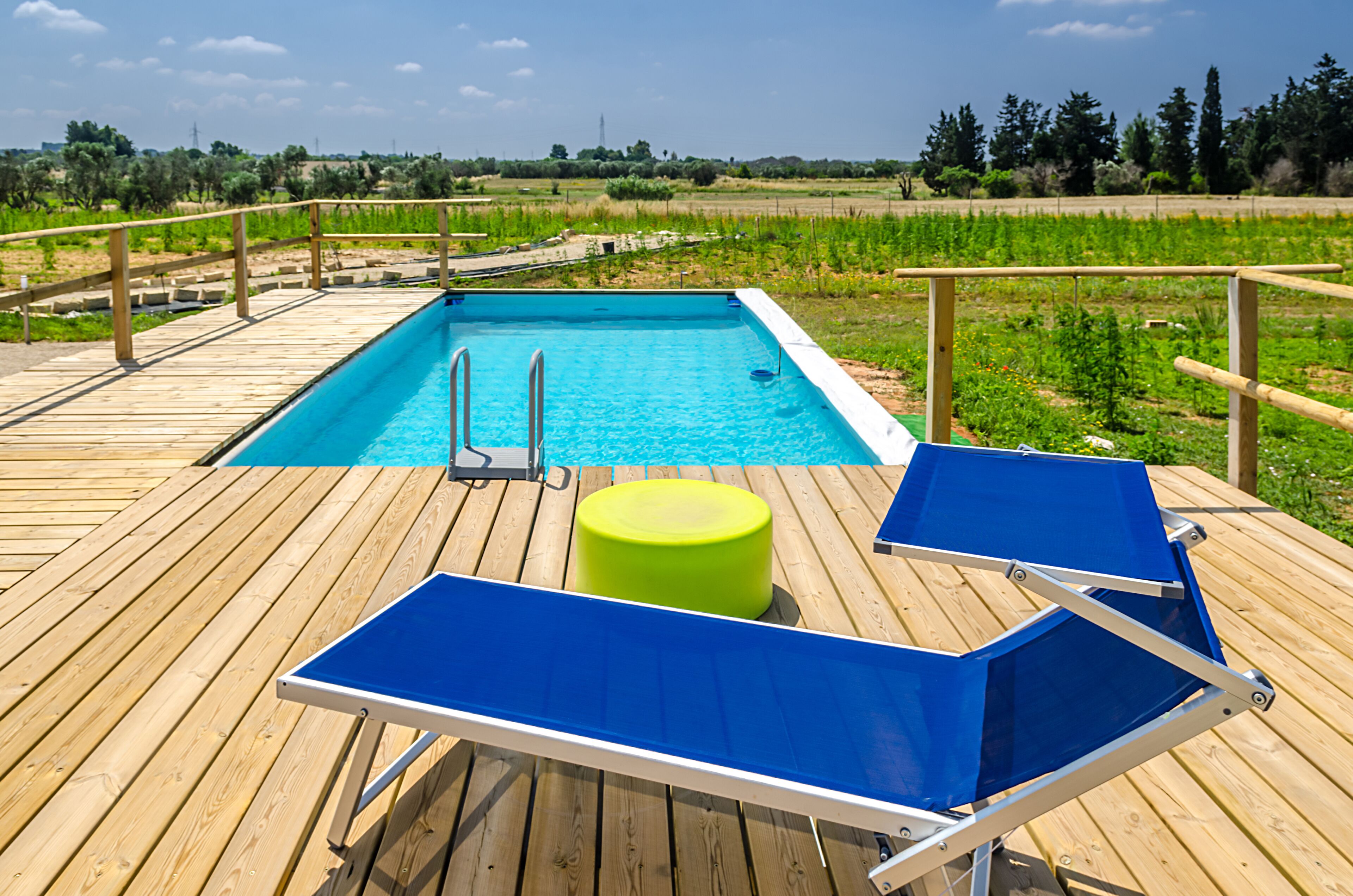 Eine Holzterrasse mit Pool, zwei blauen Liegestühlen und einem grünen Hocker.