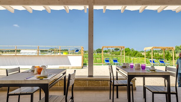 An outdoor patio with tables and chairs, overlooking a beach and pool area. - Tenuta Libò (Alezio)