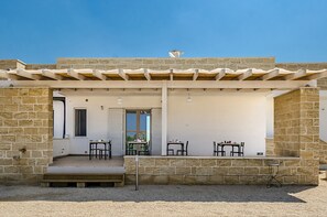 A stone building with a covered patio area, featuring outdoor seating and a small table. - Tenuta Libò (Alezio)