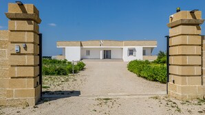 A building with a simple, modern design, featuring a central entrance flanked by two stone pillars. - Tenuta Libò (Alezio)
