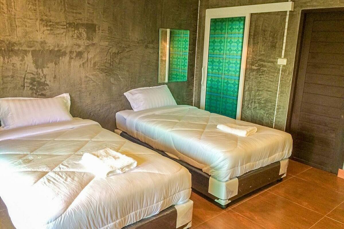 A room with two beds, a large mirror, and a green patterned window.