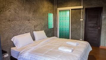 A neatly made bed with white linens and two pillows, a wall-mounted air conditioner, and a door with a geometric pattern.