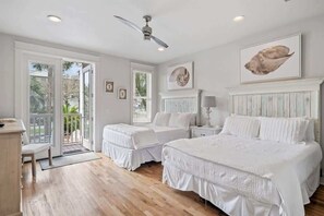 Quarto com duas camas, ventilador de teto e uma janela grande com persianas.
