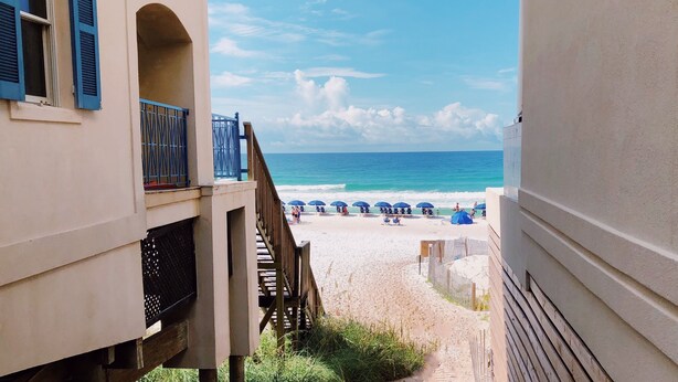 A beach view from a building with a balcony, a wooden staircase, and a fence enclosing the beach area. - 2min Walk to Private Beach! 3BR Gorgeous Townhome! (Miramar Beach)