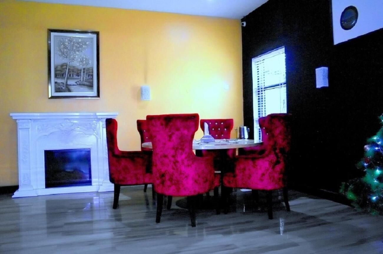 A dining area with a white fireplace, red upholstered chairs, a small table, and a Christmas tree.