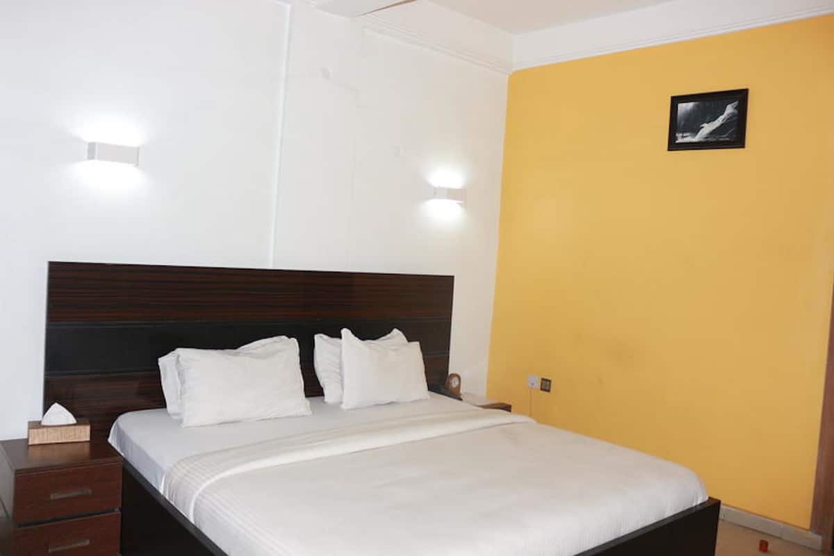 Habitación de hotel con cabecera de madera, ropa de cama blanca y una lámpara de pared.