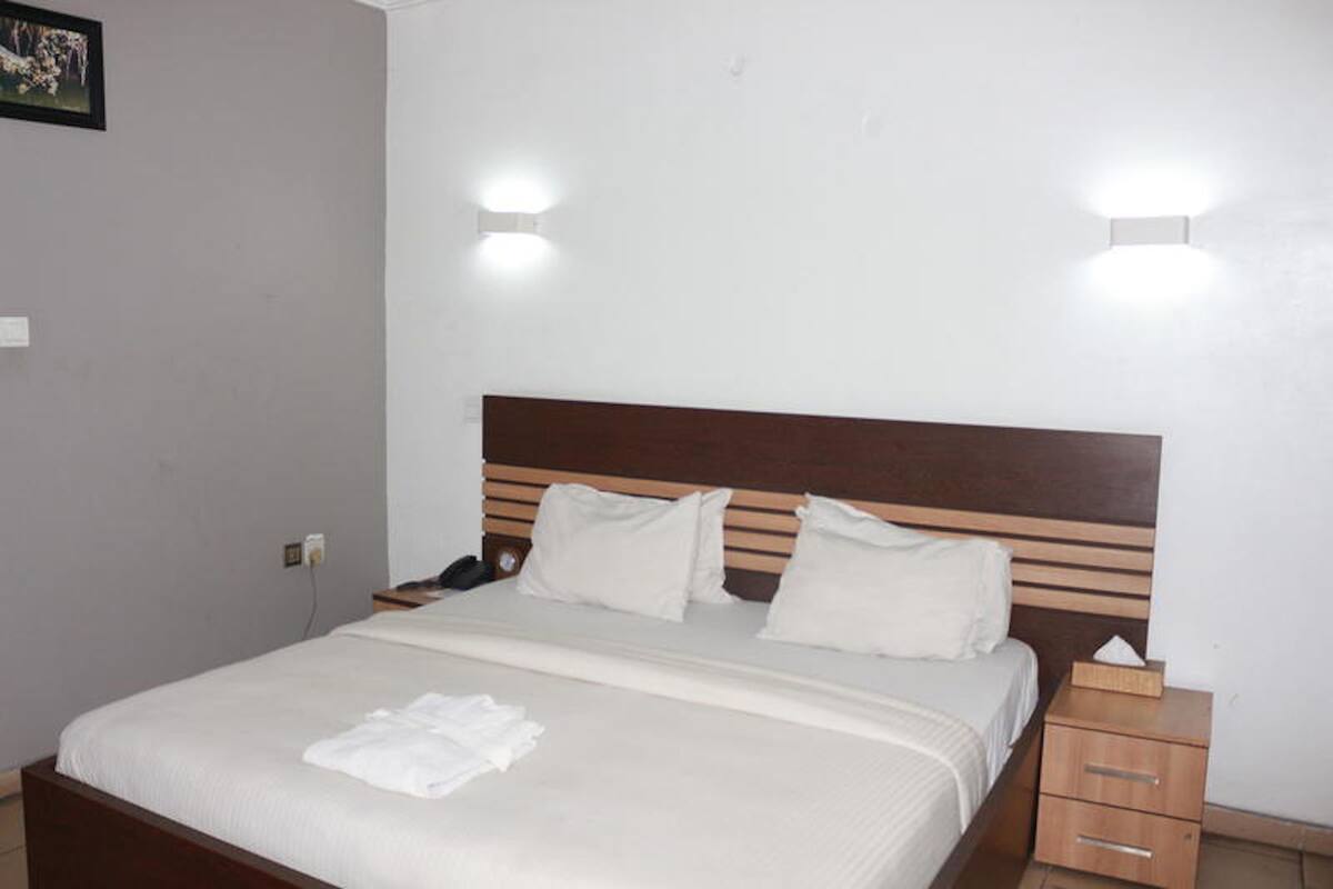 Una cama bien hecha con sábanas blancas, un cabecero de madera y mesitas de noche con lámparas.