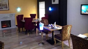 Un comedor con chimenea, sillas tapizadas en rojo, una mesa con una bebida y un televisor en la pared.