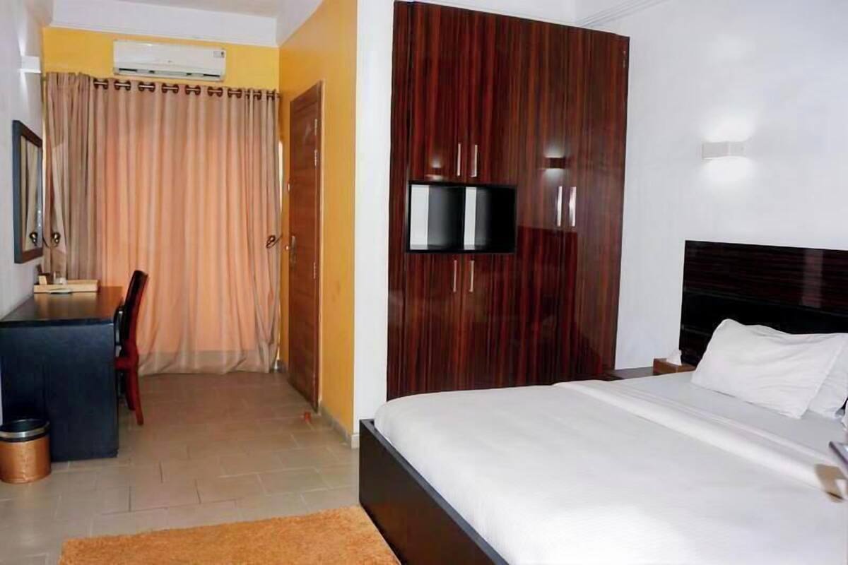 Una habitación de hotel con una cama, un escritorio, una silla, un televisor y un armario.