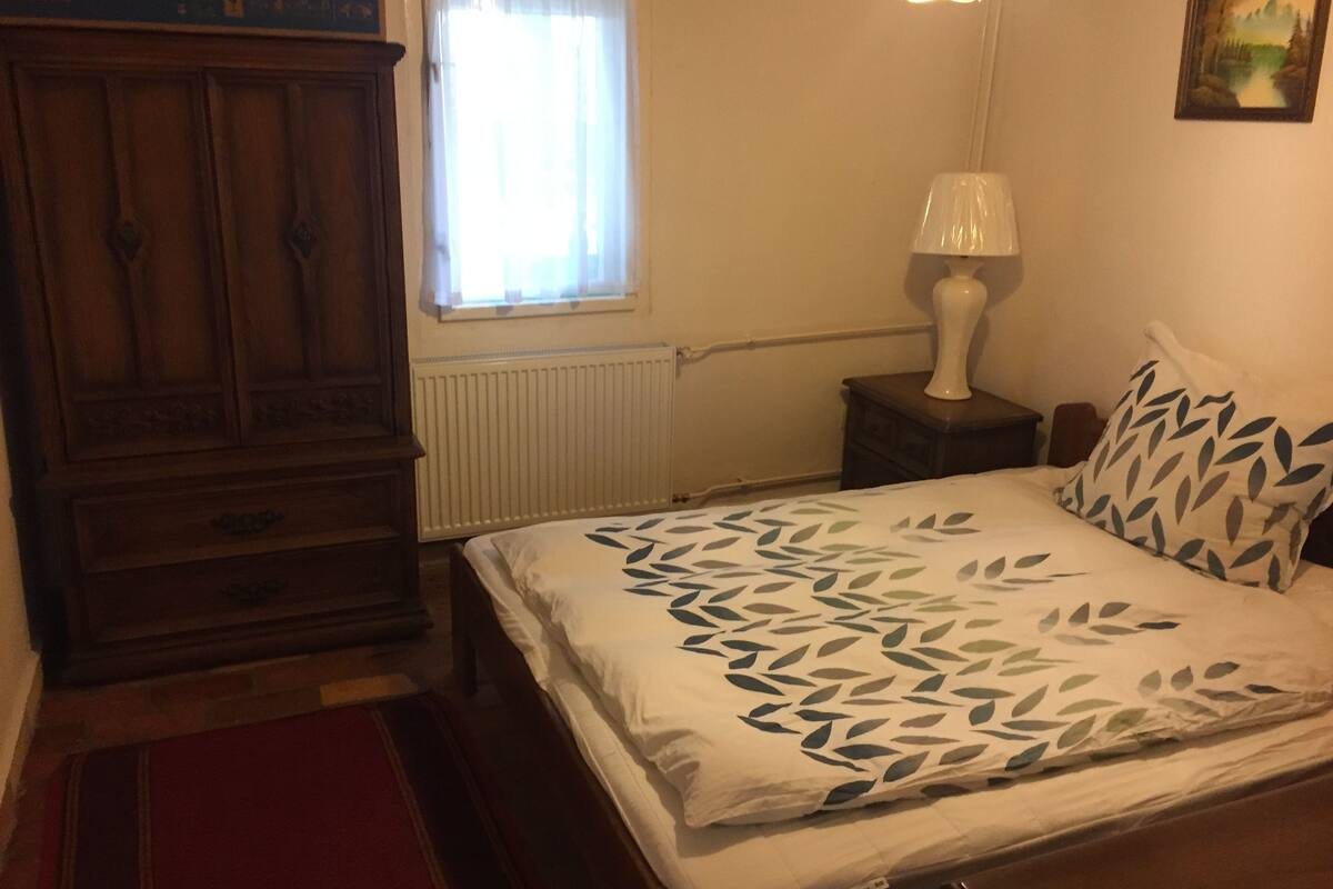 A bedroom with a bed, a nightstand, a lamp, a dresser, and a window.