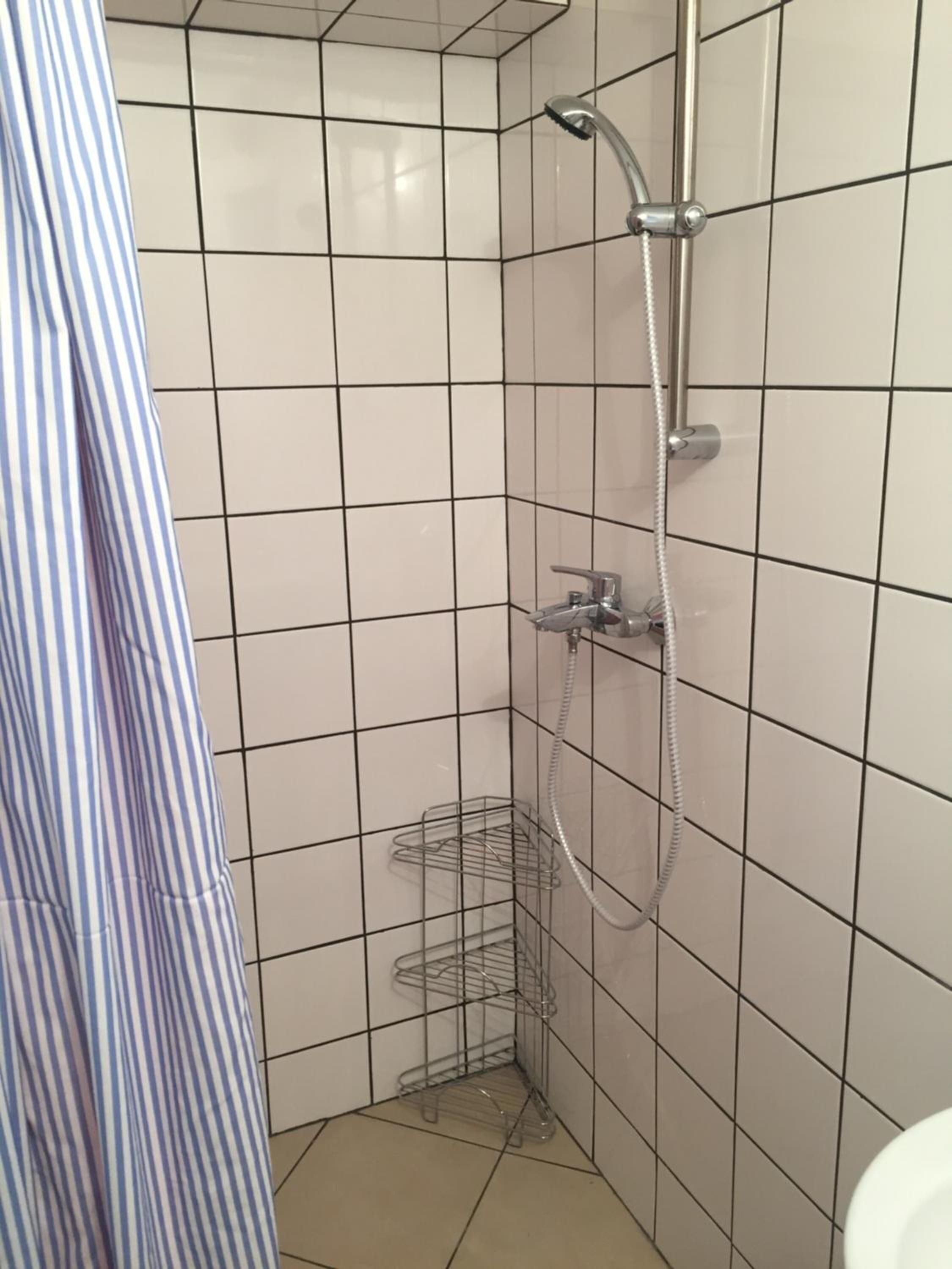 A small, tiled shower area with a handheld showerhead and a wall-mounted faucet.