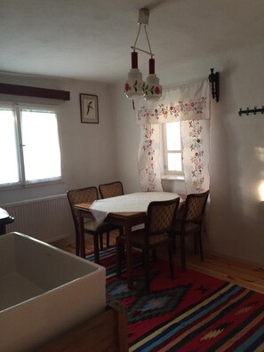 A dining area with a table and chairs, a radiator, a window with curtains, and a hanging light fixture.
