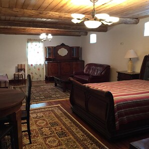 A traditional room with a wooden ceiling, a bed with a striped bedspread, a leather armchair, a wooden cabinet, and a dining table with chairs.