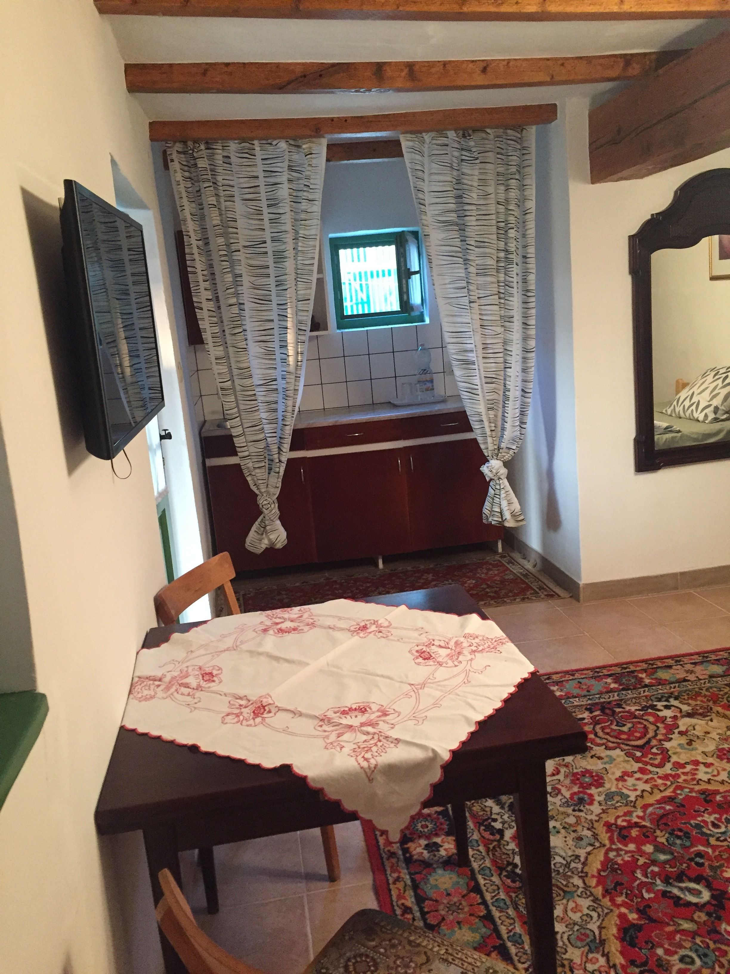Ein Essbereich mit Tisch, bedeckt mit einer blumigen Tischdecke, einem Holzbstuhl, einem gemusterten Teppich und einem Fenster mit Vorhängen.