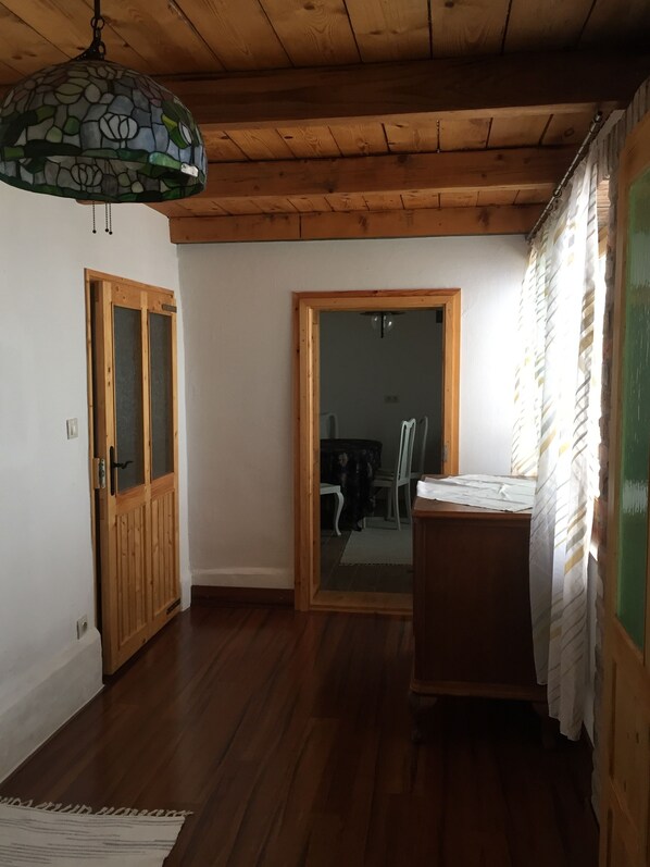 A room with wooden flooring, a stained glass ceiling light, a wooden door, and a small table with a white cloth.