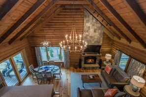 Cozy cabin interior with a high ceiling, exposed beams, and a stone fireplace. Enjoy the views of the surrounding landscape from the large windows.