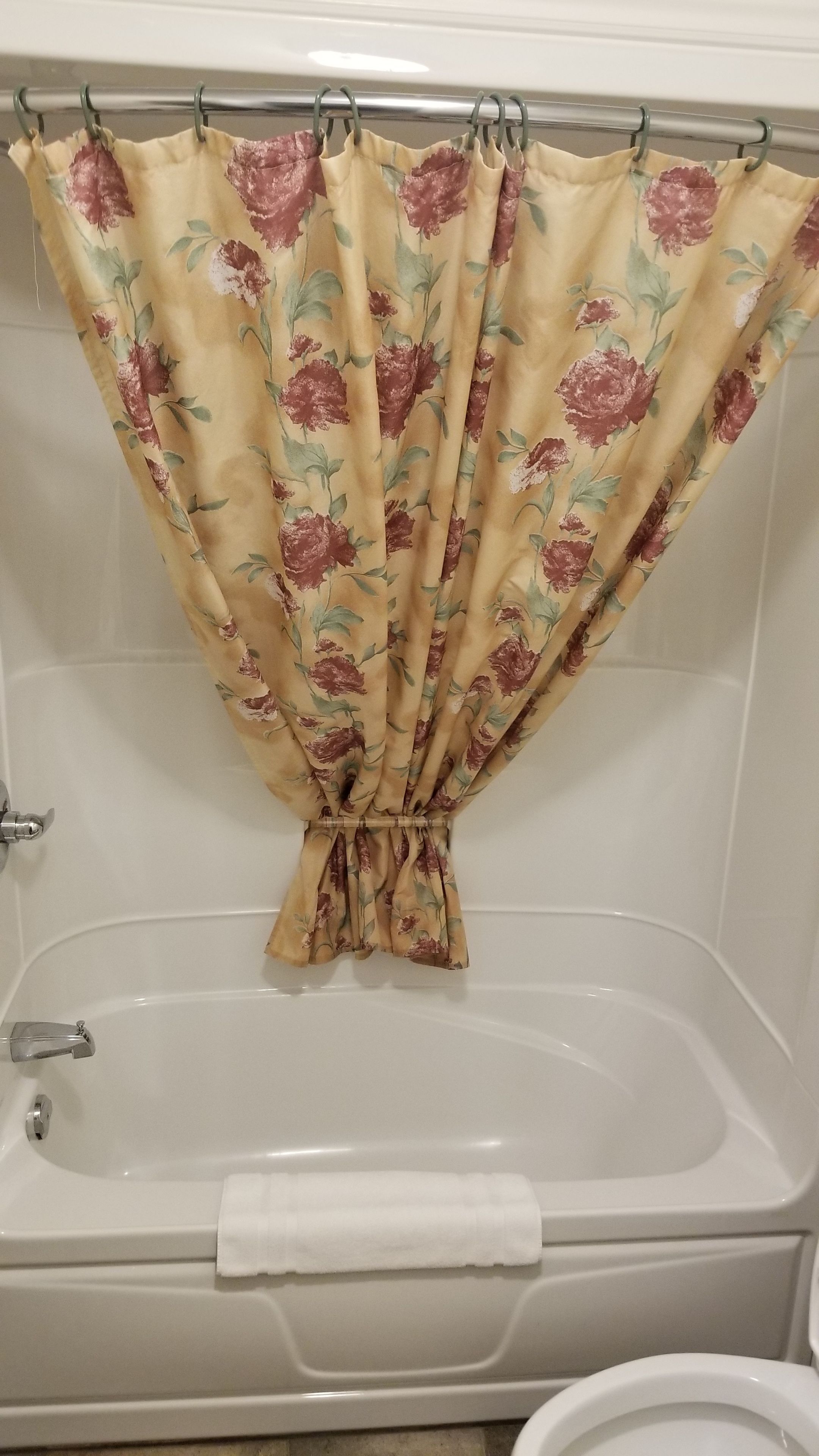 A bathroom with a bathtub, a shower curtain with a floral pattern, and a white towel on the tub.