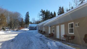 A row of single-story cabins with a covered walkway, snow on the ground, and trees in the background.