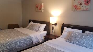 Ein Hotelzimmer mit zwei Betten, jeweils mit gemusterten Bettdecken und passenden Kissen, einem Nachttisch mit einer Lampe sowie floralen Bildern an den Wänden.
