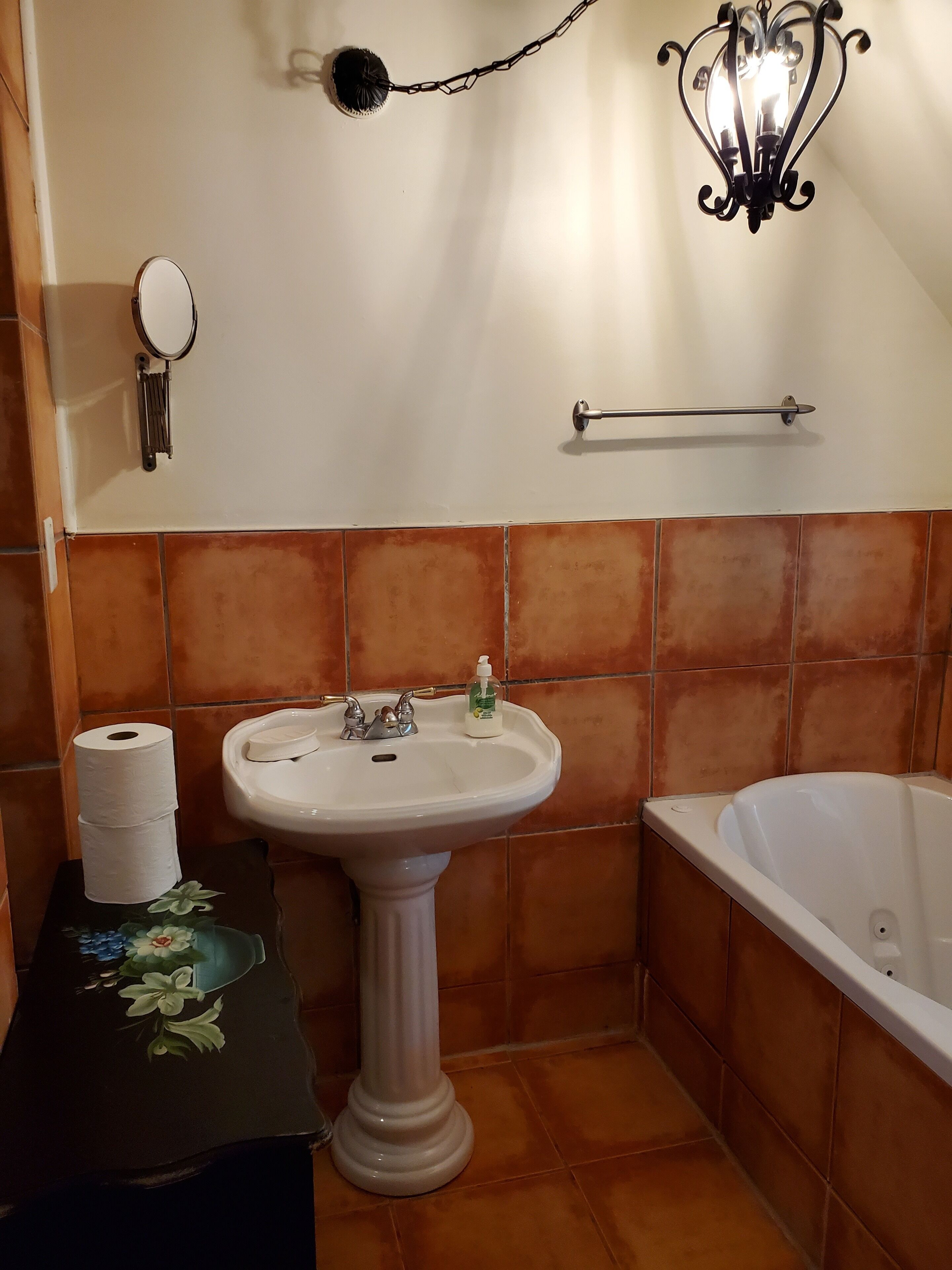 Un baño con lavabo pedestal, dispensador de jabón, perchero para toallas, porta papel higiénico y bañera.
