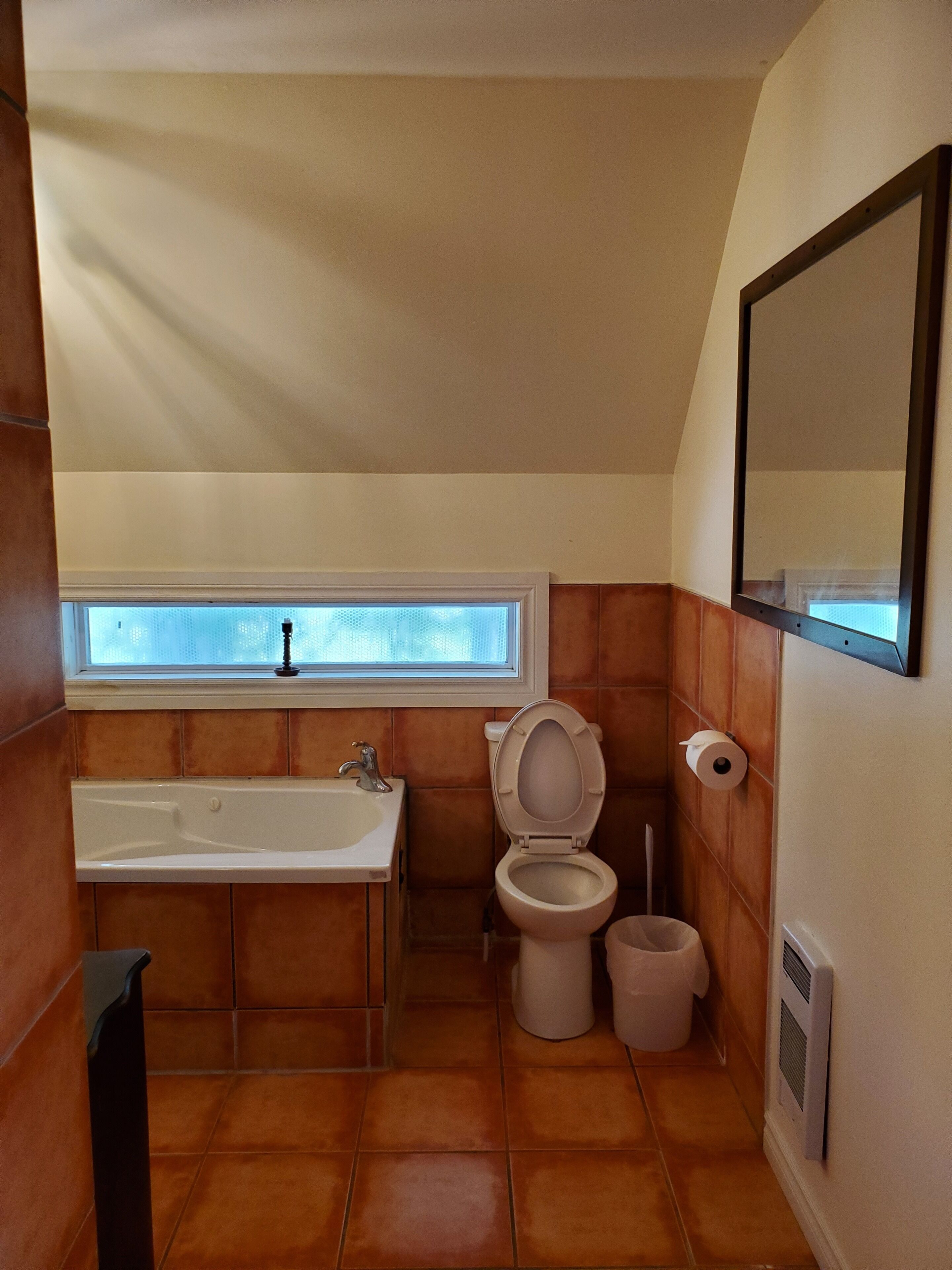 A bathroom with a bathtub, toilet, and a window above the sink.